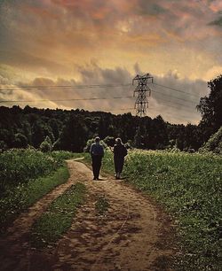 People walking on field against cloudy sky