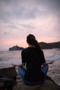 Rear view of woman doing yoga on rock at beach during sunrise