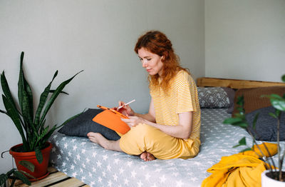 Woman working from home on bed using graphics tablet for design and drawing