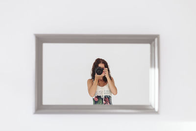 Portrait of woman photographing against white wall