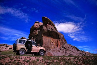 Off-road vehicle by rock formation against sky