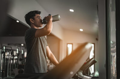 Young man drinking water while exercising in gym