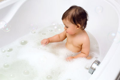 Baby boy sitting in bath with water and foam