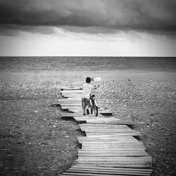 Rear view of boy on steps by sea against sky