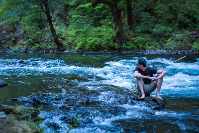 Young man sitting by river in forest