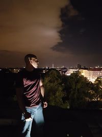 Young man sitting in city against sky at night
