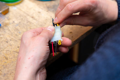 Young man's hands hold multicolored wires over desk with tools