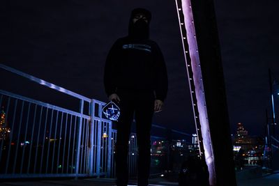 Rear view of silhouette man on illuminated bridge at night