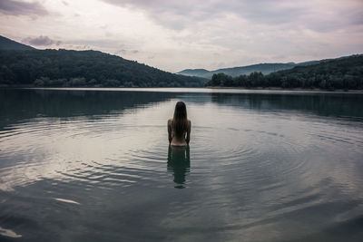 Young woman standing in lake against sky during sunset