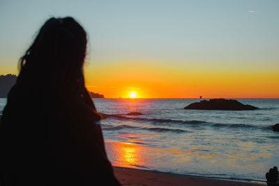 Rear view of woman looking at sea against sky during sunset