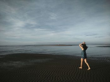 Side view of young woman walking at beach against sky during sunset