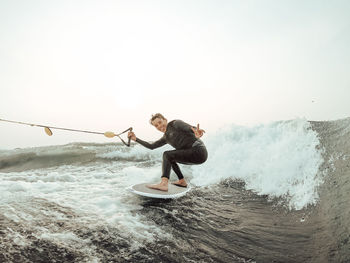 Full length of man splashing water in sea against clear sky