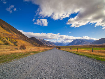Empty road amidst land and mountains against sky