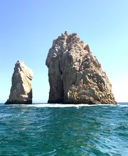 Rock formation in sea against clear blue sky