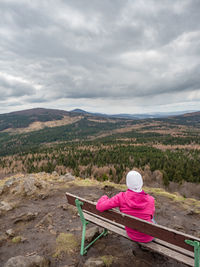 Rear view of woman sitting on landscape against sky