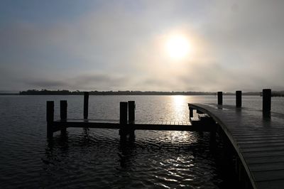 Wooden posts in sea against sky during sunset
