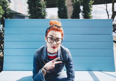 Portrait of redhead young woman gesturing peace sign while sitting on bench