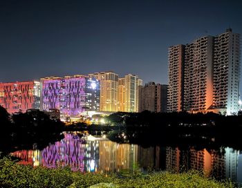 Illuminated buildings by river against clear sky at night