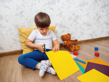 Toddler boy learns to cut colored paper with scissors. kid sits on floor in kids room 