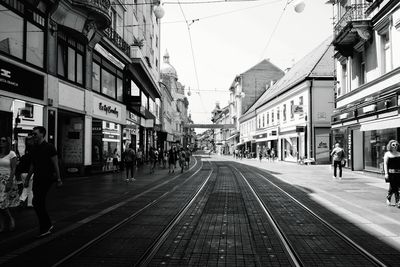 People on railroad tracks in city against clear sky