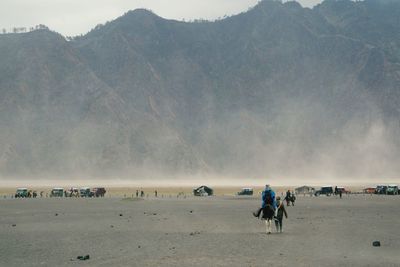 People riding horse at beach against mountains