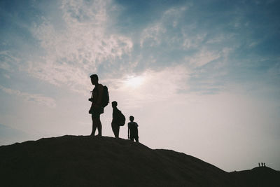 Low angle view of silhouette friends standing on rock formation against sky