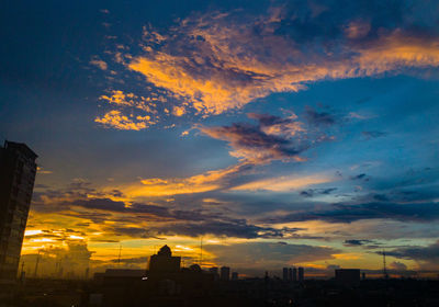 Silhouette of city against cloudy sky during sunset