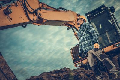 Man standing by earth mover against sky