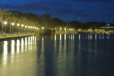 Illuminated street lights by river against sky at night