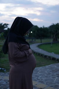 Side view of woman standing at shore against sky