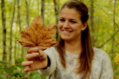 Portrait of young woman holding dry leaf while standing in forest