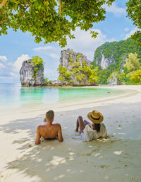 Rear view of woman sitting on beach against sky