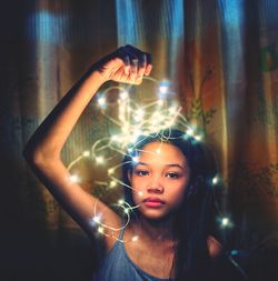 Portrait of young woman standing against illuminated wall