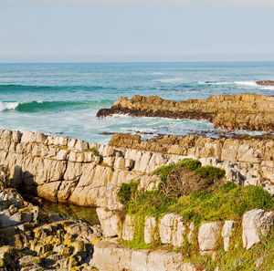 Scenic view of rocks by sea against sky