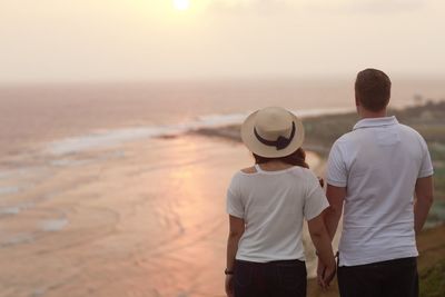 Rear view of couple standing on cliff against sky