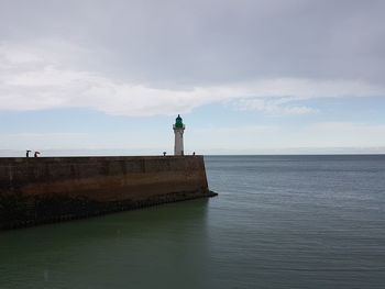 Lighthouse on sea by building against sky