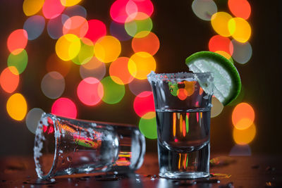 Close-up of tequila in shot glass on table against lens flares