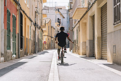 Back view of unrecognizable african american male teenager in headphones riding bmx bike in sunshine in neighborhood