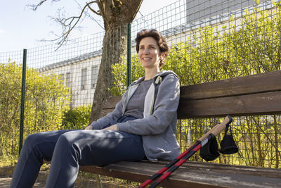 Smiling with teeth woman sits on bench holding poles after nordic walking. beautiful happy caucasian
