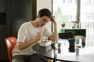 Upset man leaning on elbow having meal while sitting at table in home