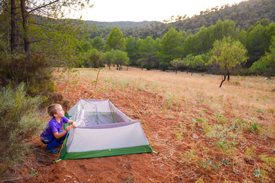 Side view of boy installing tent on land in forest