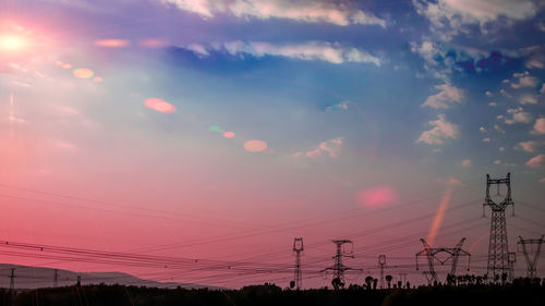 Low angle view of electricity pylon against sky during sunset