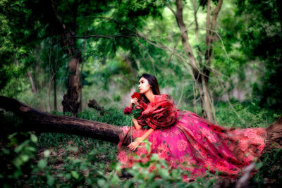 Portrait of young woman sitting on tree in forest