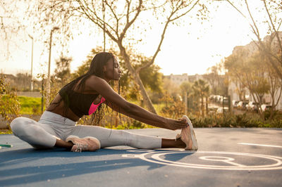 Full length of young woman exercising while sitting on land against trees