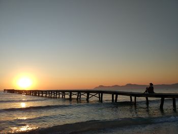 Silhouette woman sitting on pier over sea against clear sky