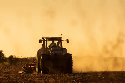 Tractor on agricultural field against sky during sunset