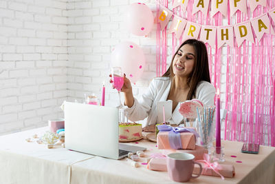 Young woman using mobile phone while sitting on birthday table having video call 