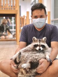 Portrait of man sitting with dog on floor covered mouth with protective face mask