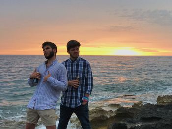 Friends standing on beach against clear sky during sunset