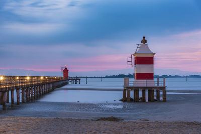Lighthouse by sea against sky during sunset